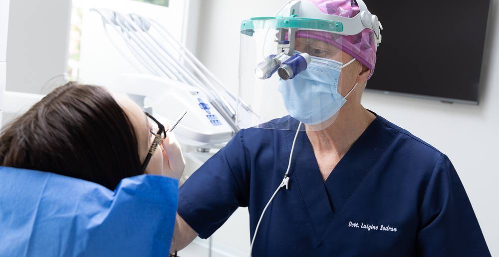 Un odontoiatra con visiera e ingranditori al lavoro